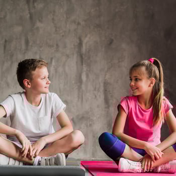 young-couple-sitting-exercise-mat-with-his-crossed-legs-looking-camera-against-concrete-wall